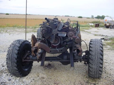 1992 Ford Bronco - The front end of a vehicle, including the engine and suspension, is shown lifted by a chain with large tires attached.