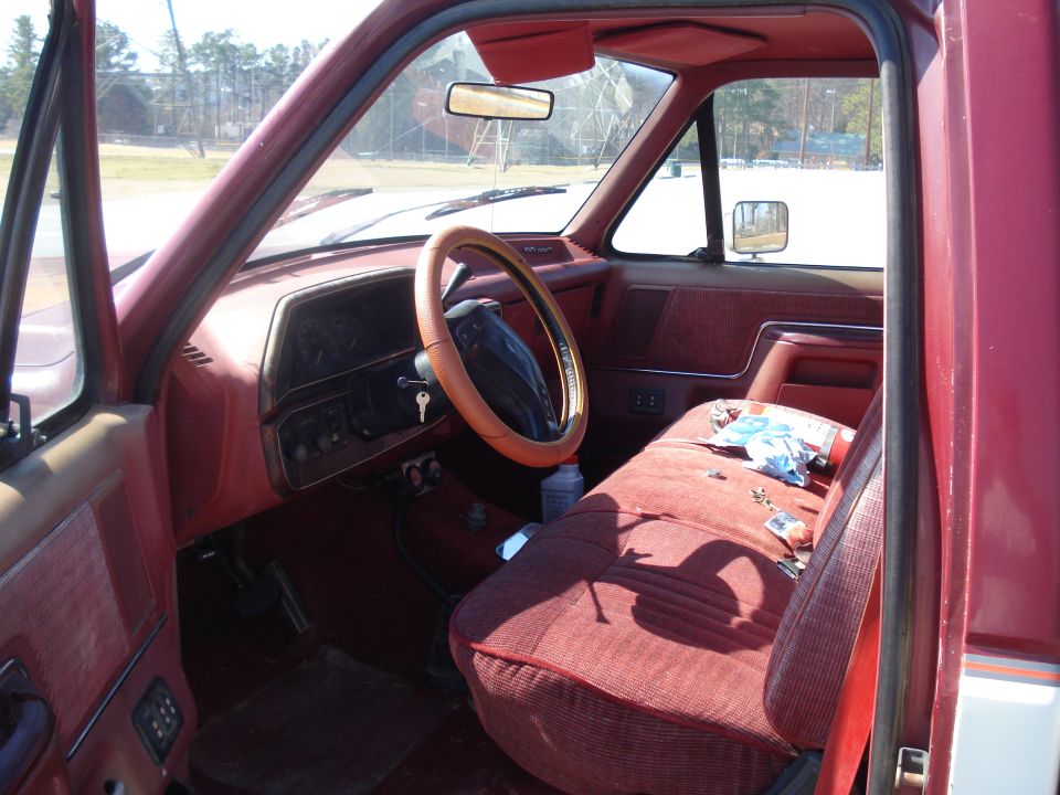 Interior of a red pickup truck, showing the dashboard, steering wheel, and passenger seat. The dashboard has a key in the ignition