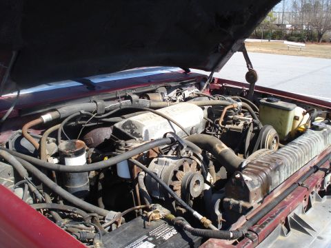 1989 Ford F-250 - The engine bay of a red truck is shown with the hood open, revealing the engine components.