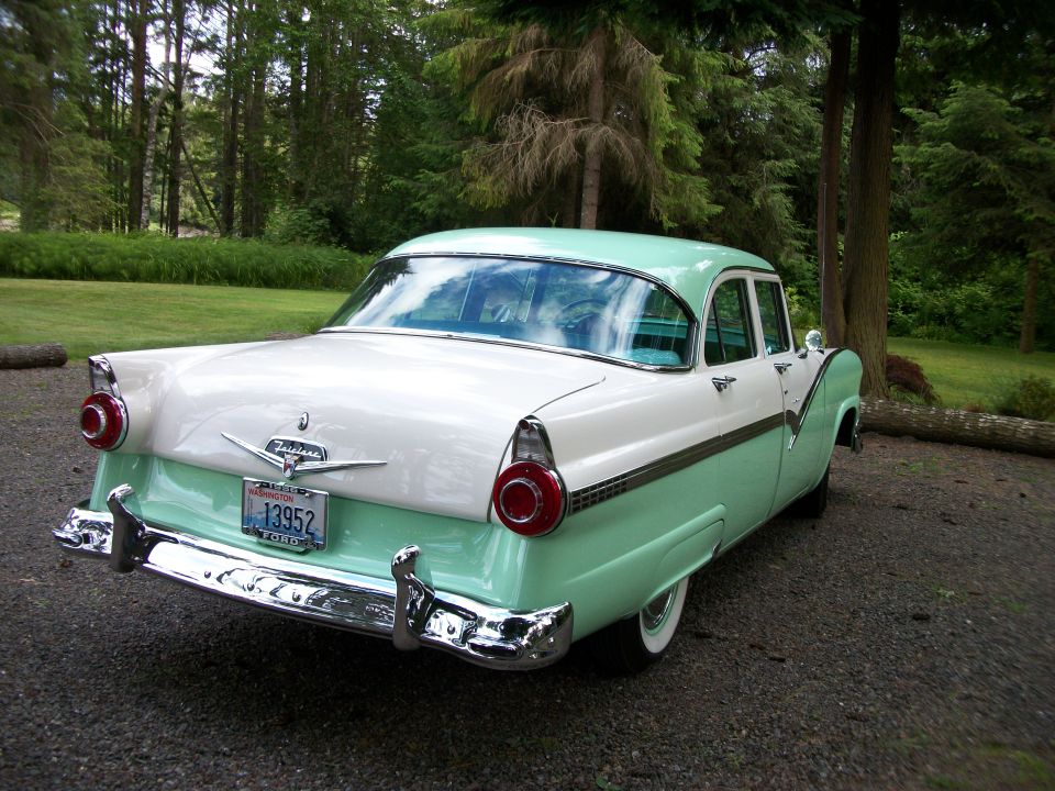 Restored green and white 1950s Ford Fairlane sedan, three-quarter rear view on gravel