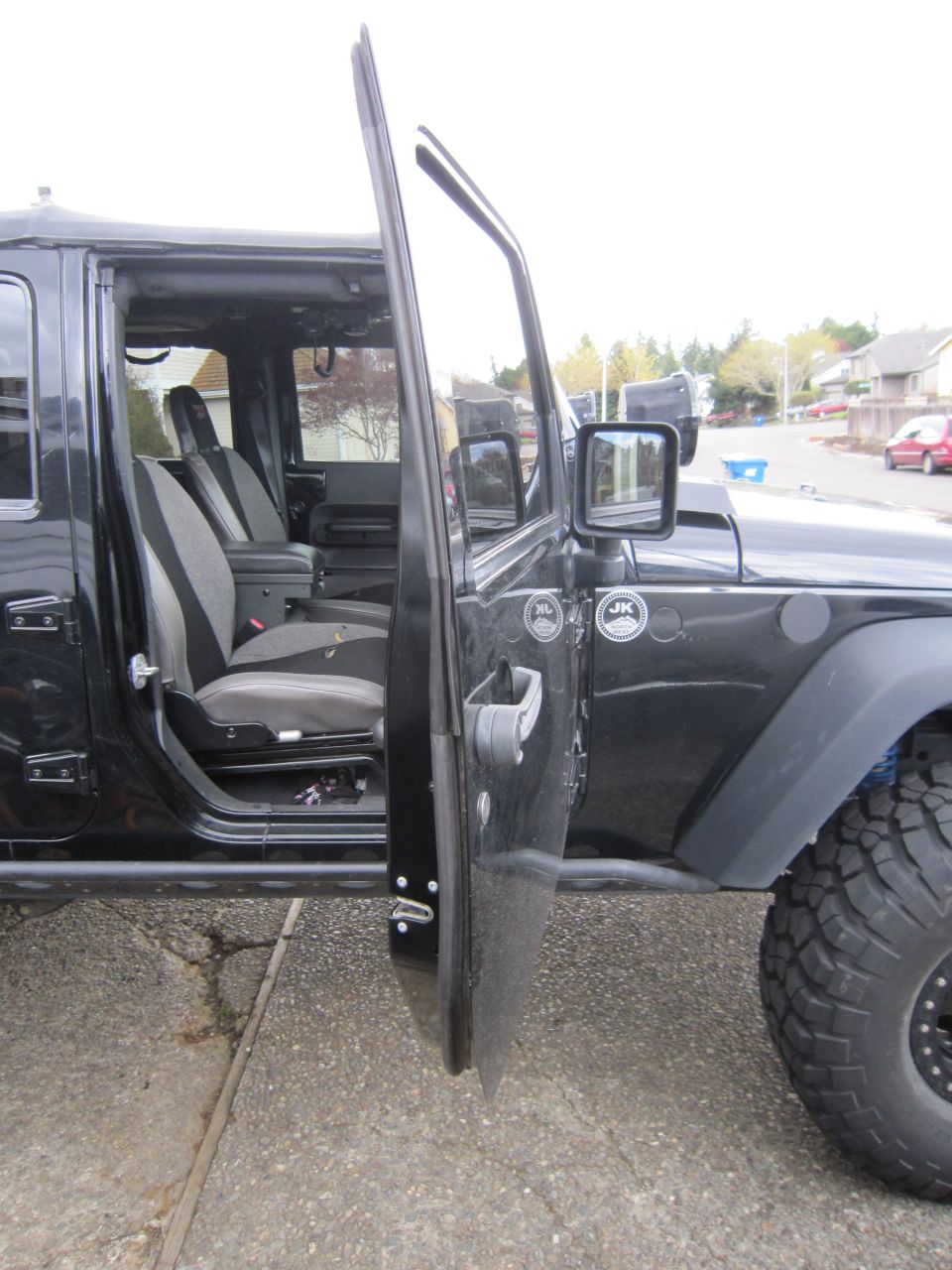 Black Jeep Wrangler with driver's door open, showing interior seats and "JK" badge on the exterior