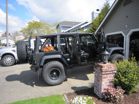 2008 Jeep Wrangler - A black Jeep Wrangler with its doors off is parked in a driveway next to a white truck.