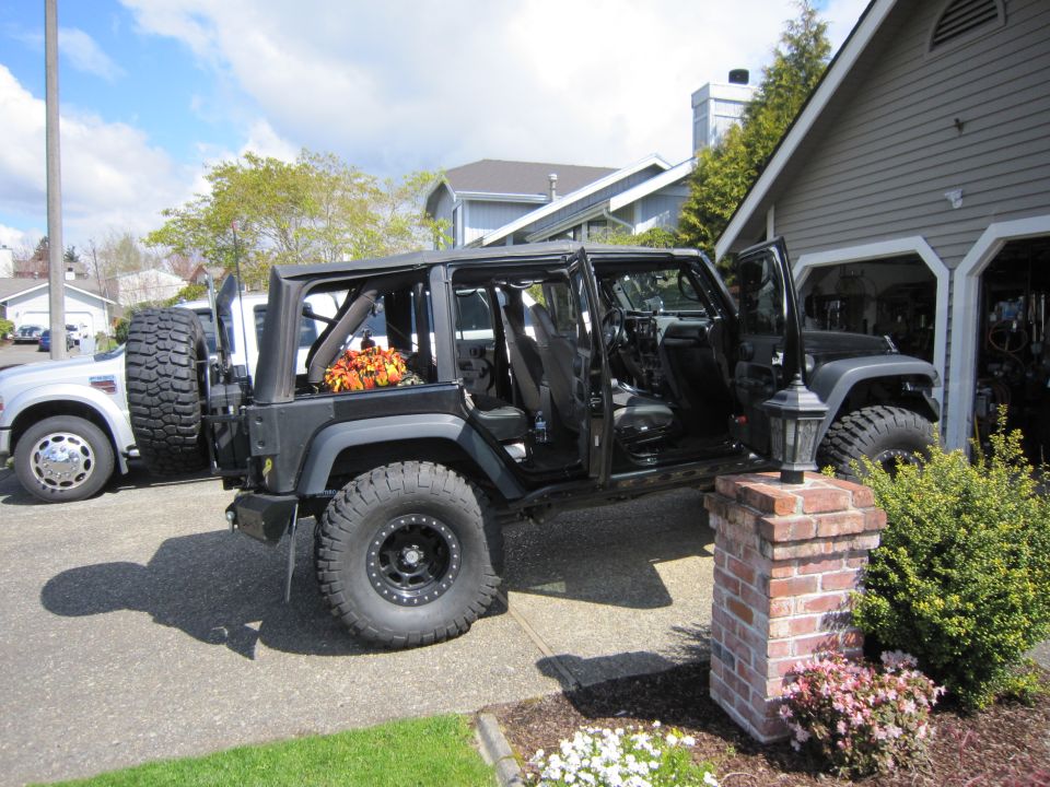 Black Jeep Wrangler with doors removed, parked next to a white truck. Fall decorations in the back seat