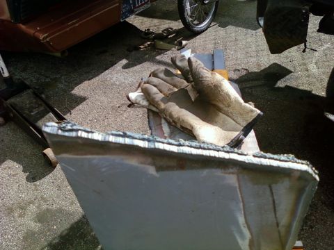 1989 Ford Bronco - A pair of worn work gloves lies on a metal car part, with other vehicles visible in the background.