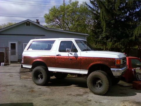 1989 Ford Bronco - This lifted Ford Bronco features a unique white and red glitter paint job and large off-road tires.