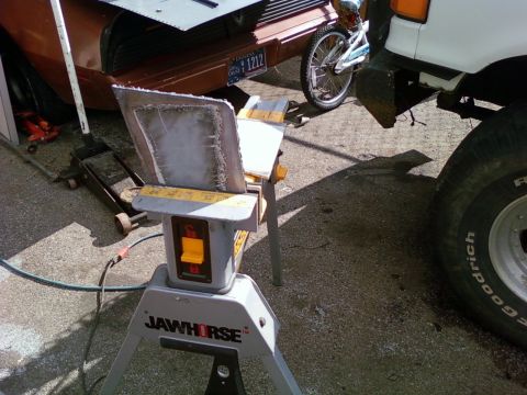 1989 Ford Bronco - A metal panel is being worked on with a Jawhorse, with a bicycle and parts of a brown car and white truck visible.