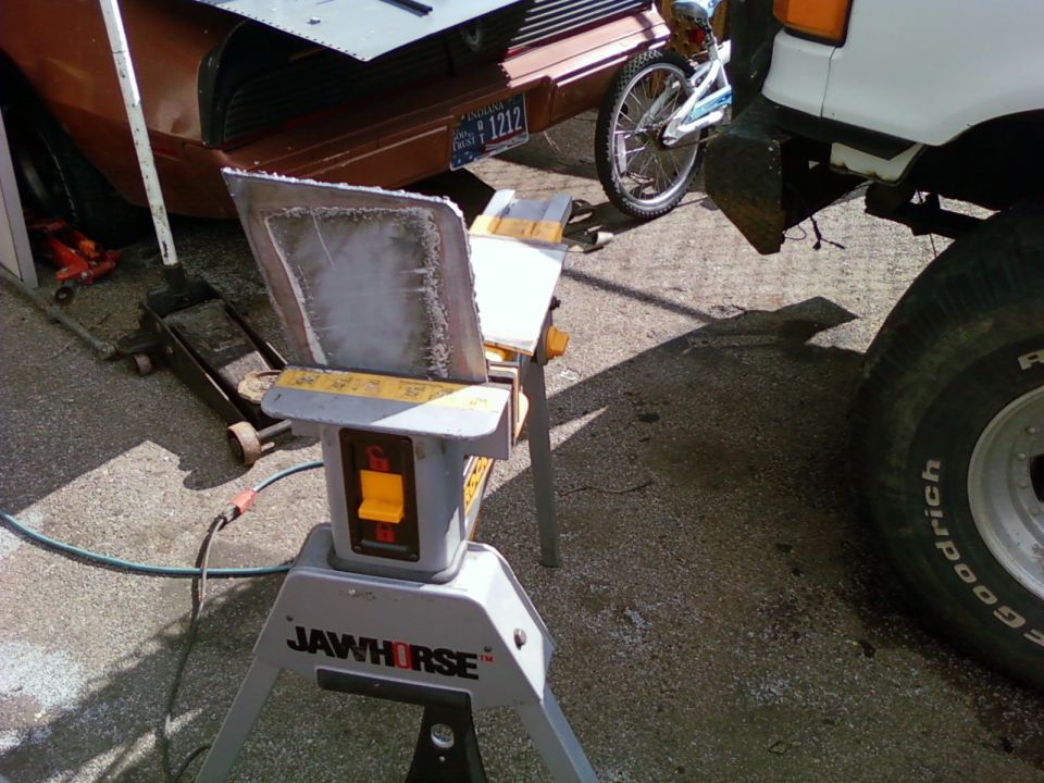 Metal panel on a Jawhorse with a bicycle and parts of two vehicles in background