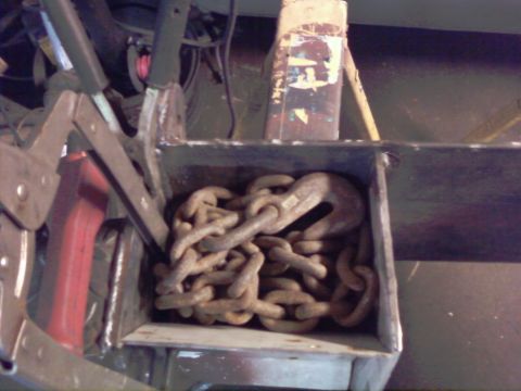 1989 Ford Bronco - Rusty chains and hooks are stored in a metal box, secured by clamps.