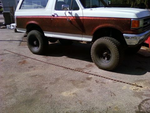 1989 Ford Bronco - A Ford Bronco with a two-tone paint job, a white top and speckled brown lower body, is parked on an asphalt surface.