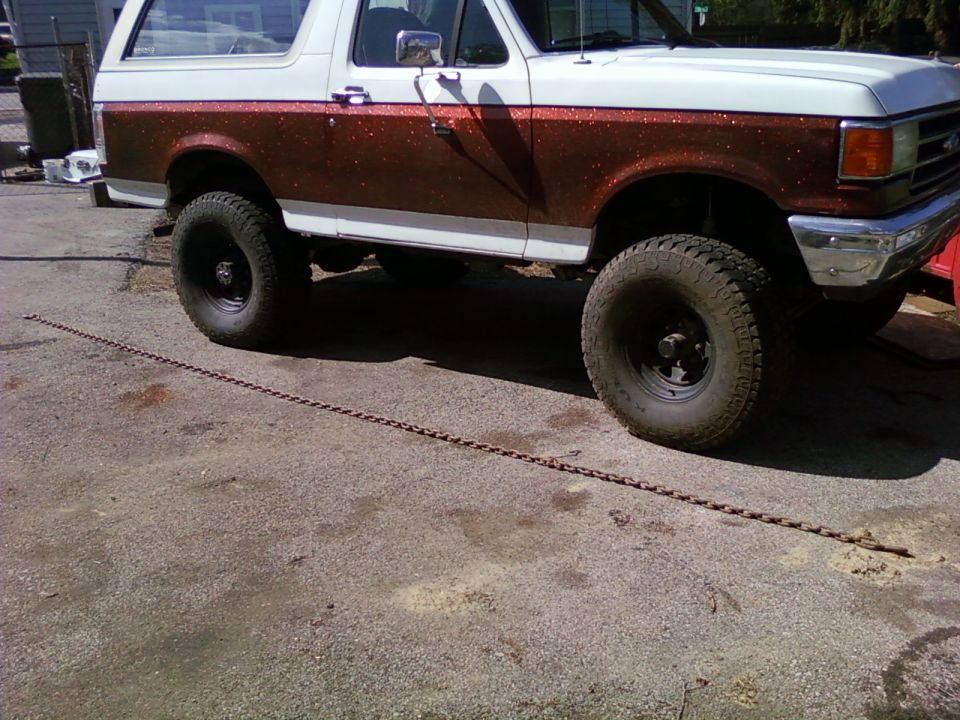 Side view of a white and brown speckled Ford Bronco with large tires