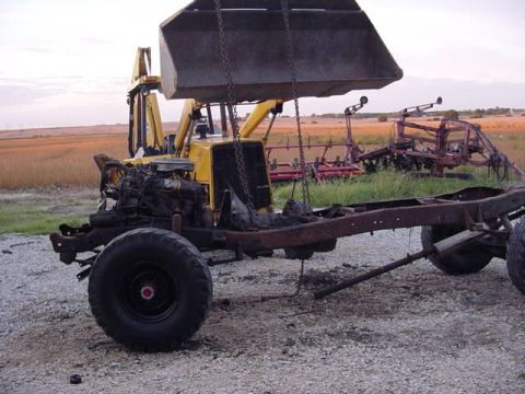 1992 Ford Bronco - A backhoe is lifting a vehicle frame that has an engine and one wheel attached.