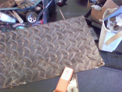 1989 Ford Bronco - A close-up of a diamond plate metal sheet, with various items and boxes visible in the blurred background.