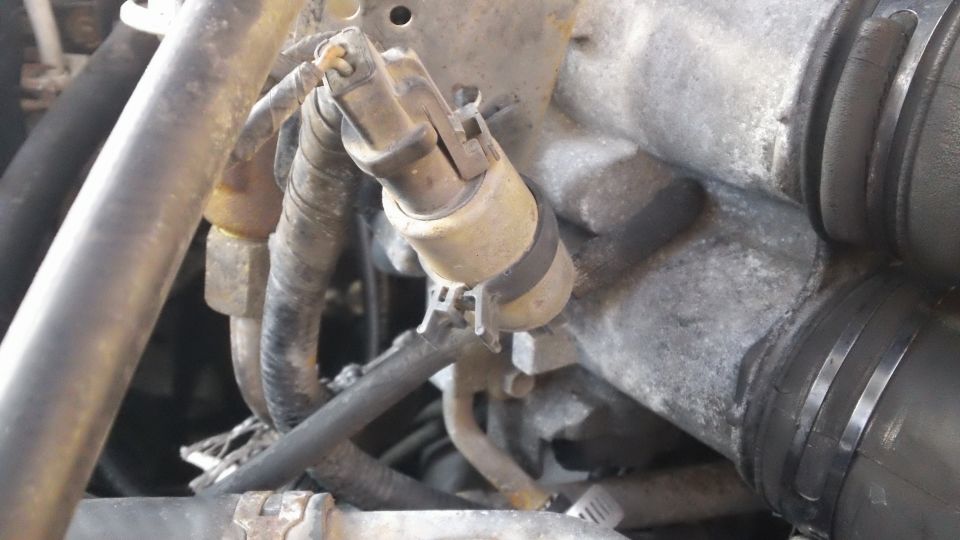 Close-up of a sensor with wires and hoses connected to an engine component