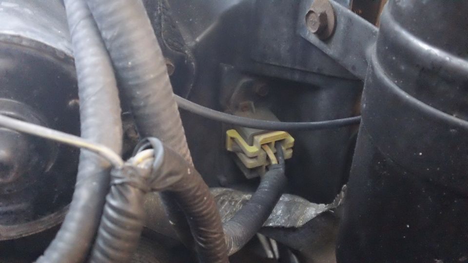 Close-up of a yellow electrical connector with wires attached, part of a vehicle's engine bay