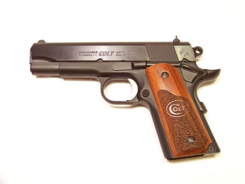 1995 Mercury Grand Marquis - A close-up view of a Colt Commander automatic pistol with textured wooden grips and the Colt logo visible.