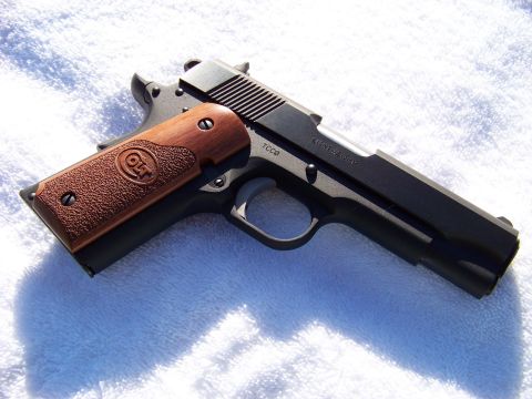 1995 Mercury Grand Marquis - A Colt 1911 pistol with textured wood grips is shown from a side angle on a white background.