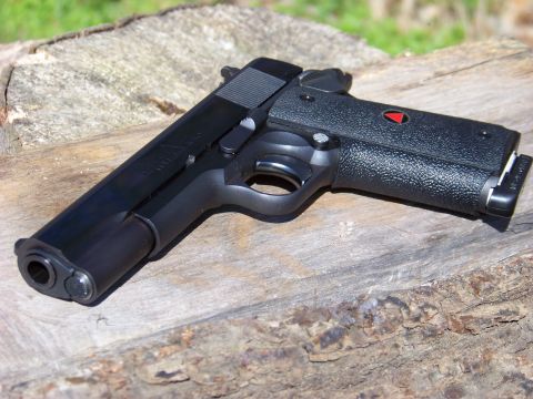 1995 Mercury Grand Marquis - Colt 1911 pistol with black textured grips and a red delta emblem is shown on a wooden surface.