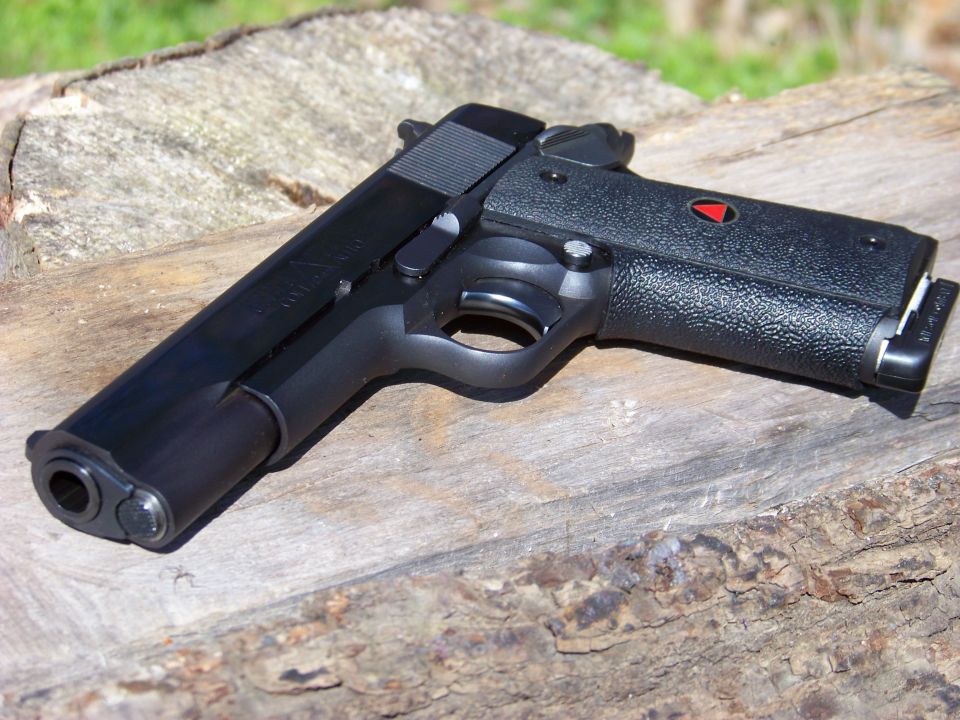Colt 1911 pistol with black grips and a red delta emblem, resting on a wooden surface