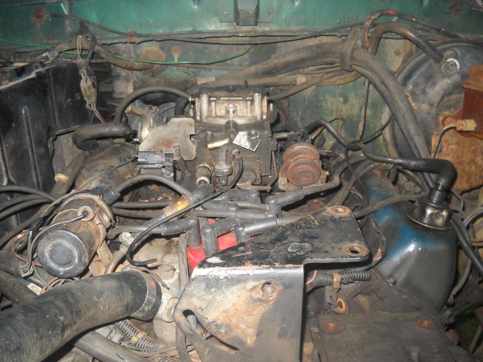 Engine bay showing a carburetor, distributor, and various hoses and wires