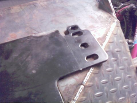 1989 Ford Bronco - A metal bracket with several holes is shown close-up on a textured surface.