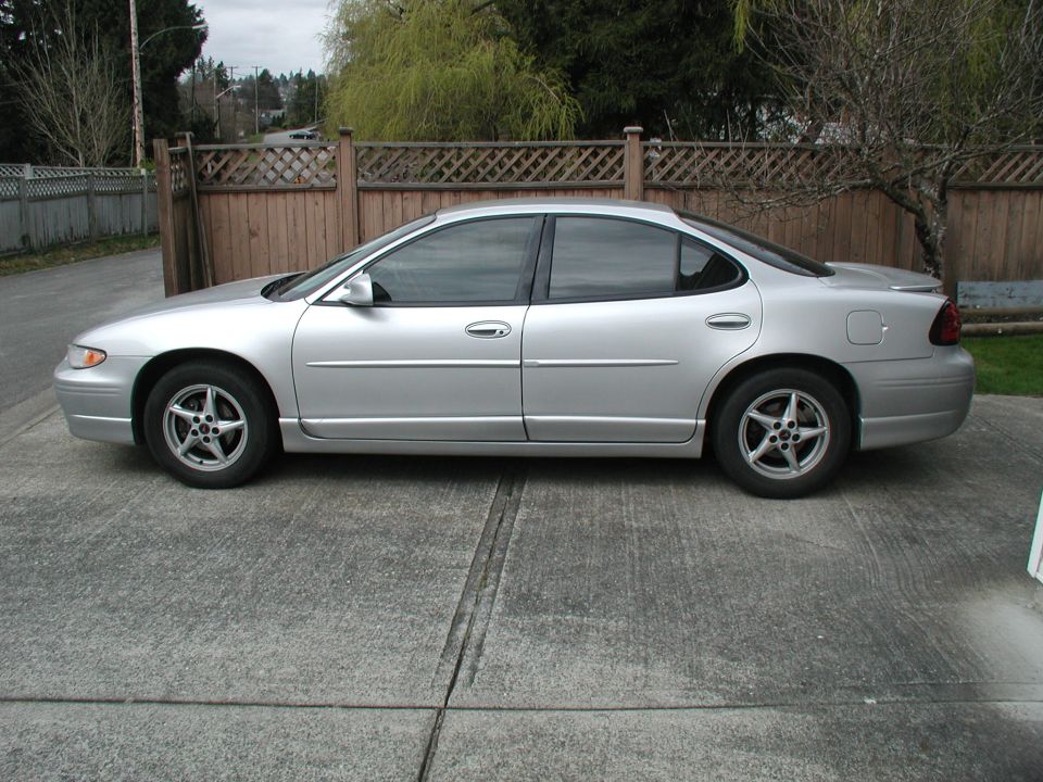 Driver-side profile of a silver Pontiac Grand Prix sedan by a fence