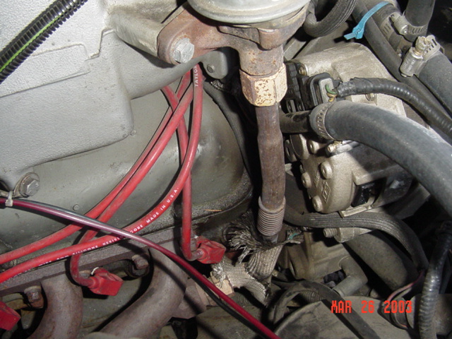 Engine bay with red plug wires, rusty rod, and black hoses; dated Mar 26 2003