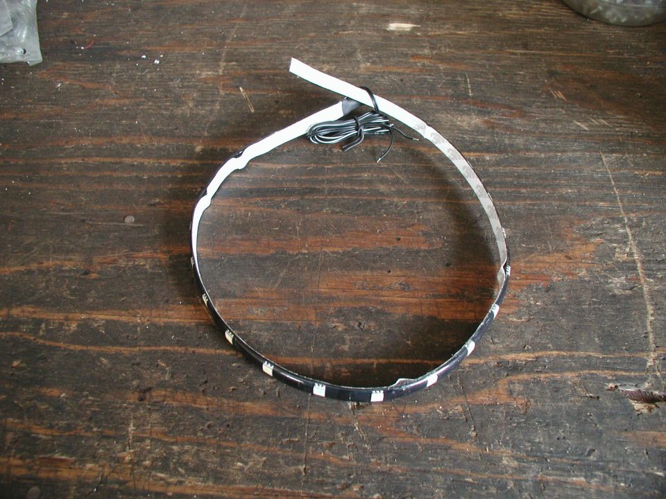 Coiled black LED strip with adhesive backing and wire lead on a wooden workbench