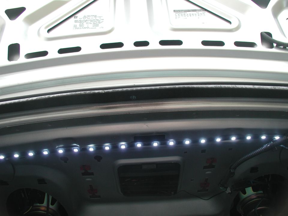 Lit white LED strip mounted along a car's trunk opening lip with lid raised