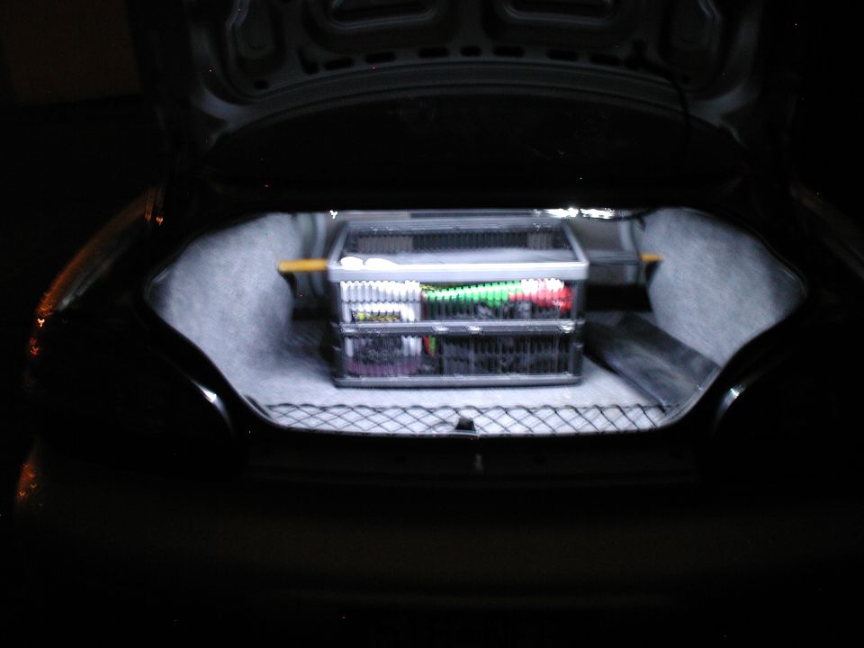 Open sedan trunk lit by bright white LED light with parts organizer bin inside