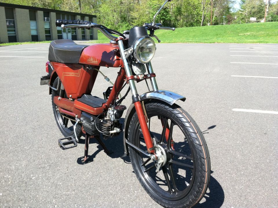 Red moped with chrome fenders and black seat parked on asphalt