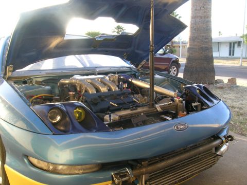 1995 Ford Probe - The engine bay of a blue car is exposed, revealing its modified components and a prominent Ford emblem.