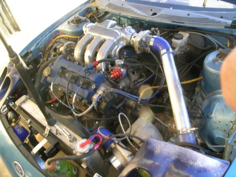 1995 Ford Probe - The engine bay of a teal car displays numerous aftermarket modifications and extensive wiring.