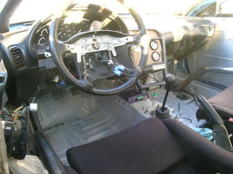1995 Ford Probe - The interior of a modified vehicle shows a roll cage, aftermarket gauges, and exposed wiring, indicating significant customization.