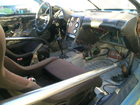 1995 Ford Probe - The interior of a car shows racing seats, a roll cage, and extensive exposed wiring, indicating modifications.