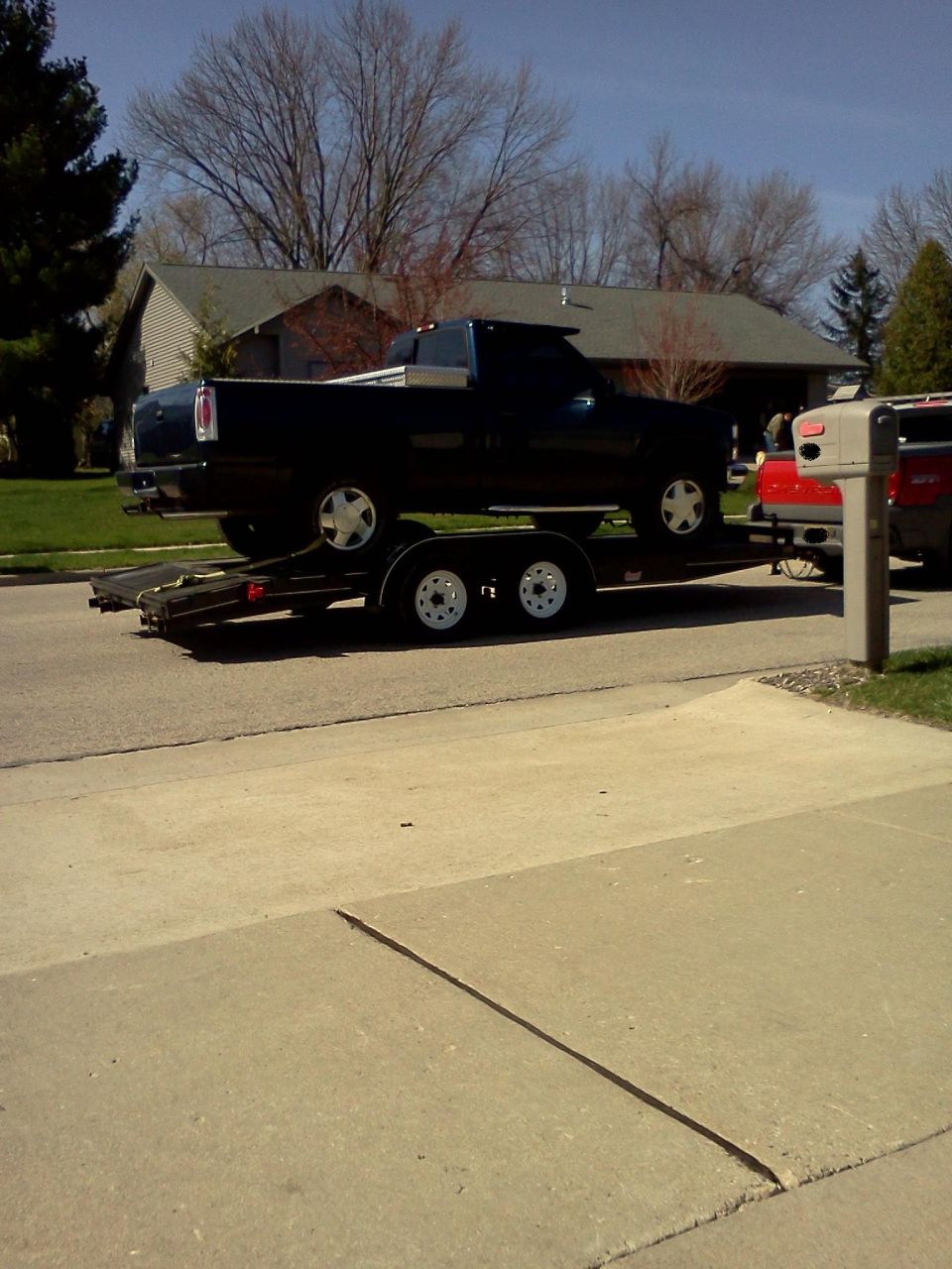 Dark blue pickup truck being towed on a trailer, with a red truck visible behind it