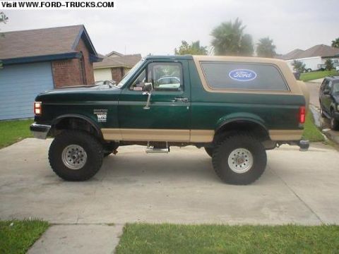 1990 Ford Bronco - A green and tan 1990 Ford Bronco is shown from the side, parked on a concrete driveway with grass in the foreground.