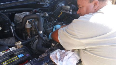 1994 Ford Bronco - A mechanic works on the engine of a vehicle, with a battery and various hoses visible.
