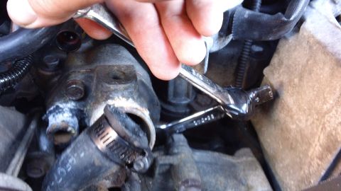 1994 Ford Bronco - Mechanic works on an engine part, using a wrench on a bolt near a hose clamp.