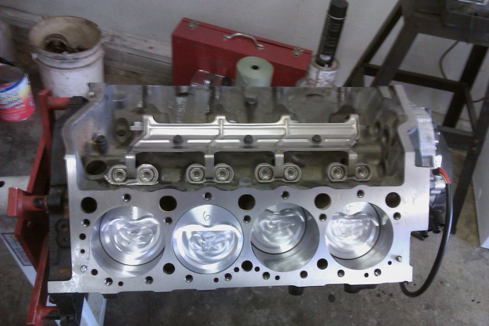 Engine block with four pistons visible, sitting on a stand. Tools and a toolbox are in the background