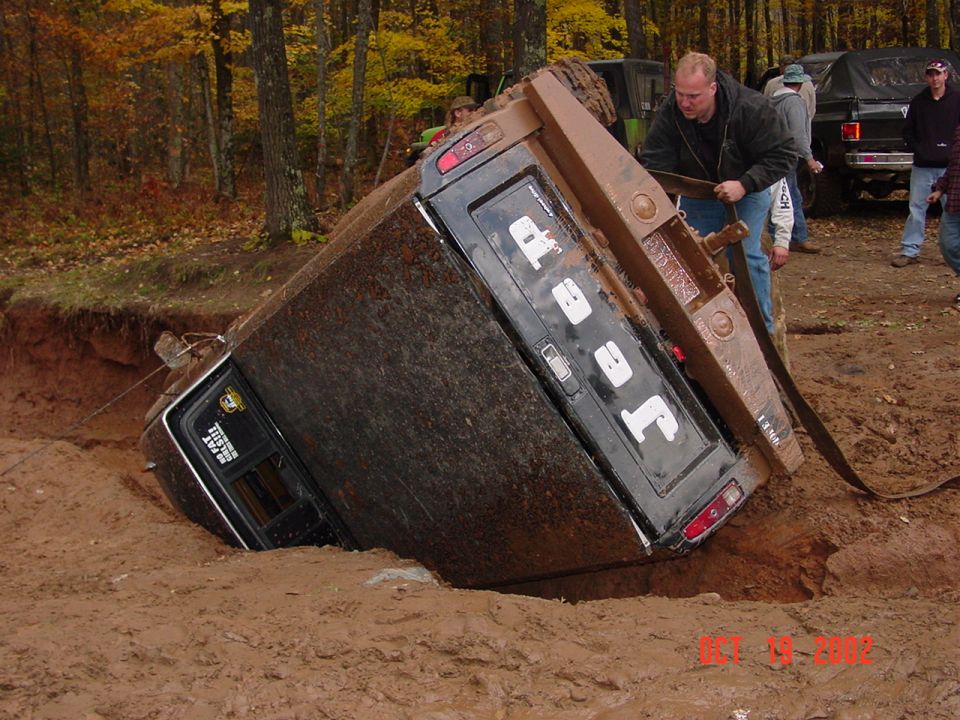 Jeep J-10 truck tipped over in a muddy hole with people trying to pull it out