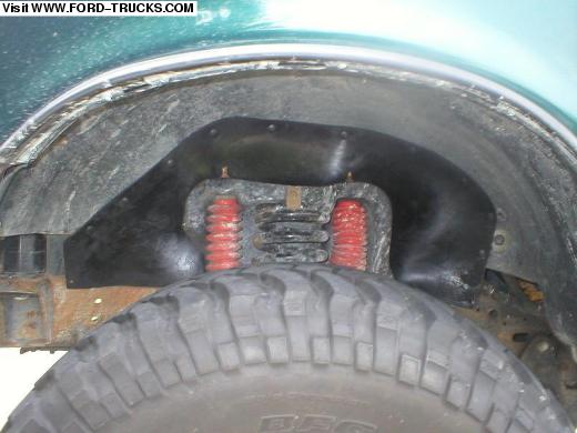 Front wheel well of a teal Ford truck with red bump stops and mud-terrain tire