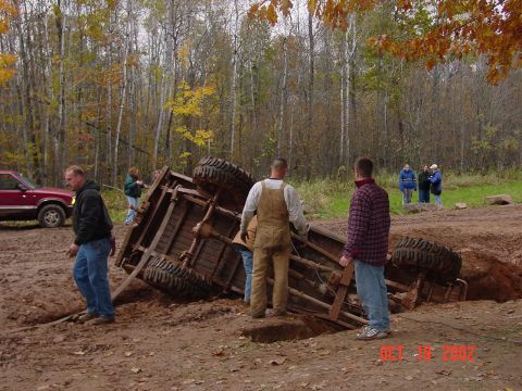 1986 Jeep J-10 - A group of people observe an overturned vehicle in a muddy off-road area during autumn.