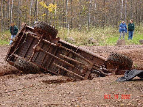 1986 Jeep J-10 - A truck has rolled onto its side in a muddy ditch, with onlookers observing the scene.