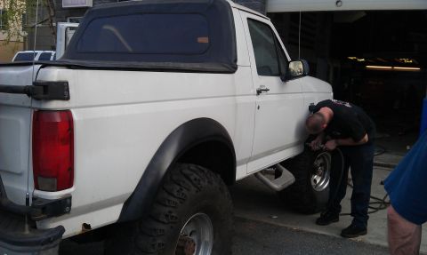 1996 Ford Bronco - A man works on the front tire of a white pickup truck with a black soft top.