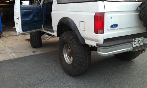 1996 Ford Bronco - This lifted Ford Bronco shows a blue interior and large off-road tires, with a visible Ford badge on the tailgate.