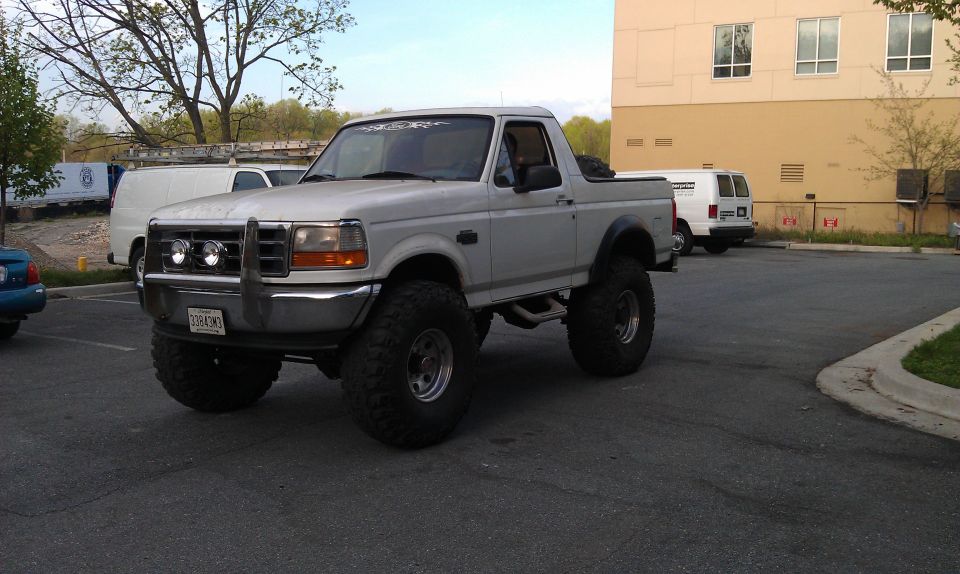 Lifted white 1996 Ford Bronco with aftermarket grille guard and large tires