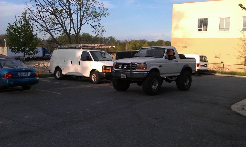 1996 Ford Bronco lifted with large tires, parked next to a white van