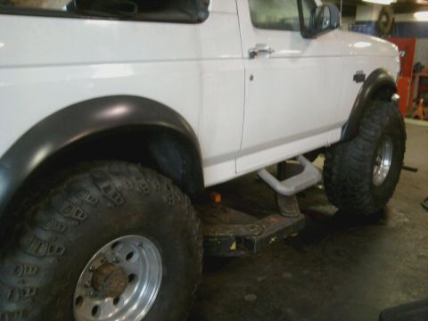 1996 Ford Bronco - This white SUV features large off-road tires and a lifted suspension, with running boards visible on the side.