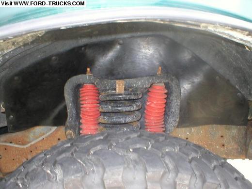 Front coil spring suspension in wheel well with red bump stops above mud tire