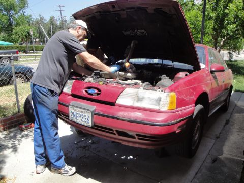 1995 Ford Taurus - Mechanic works on the engine of a red 1995 Ford Taurus with the hood open.